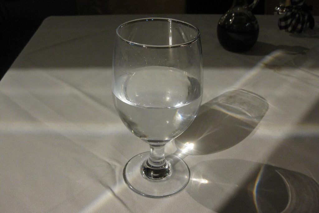 Verre d'eau à pied posé sur une nappe blanche dans la lumière du jour
