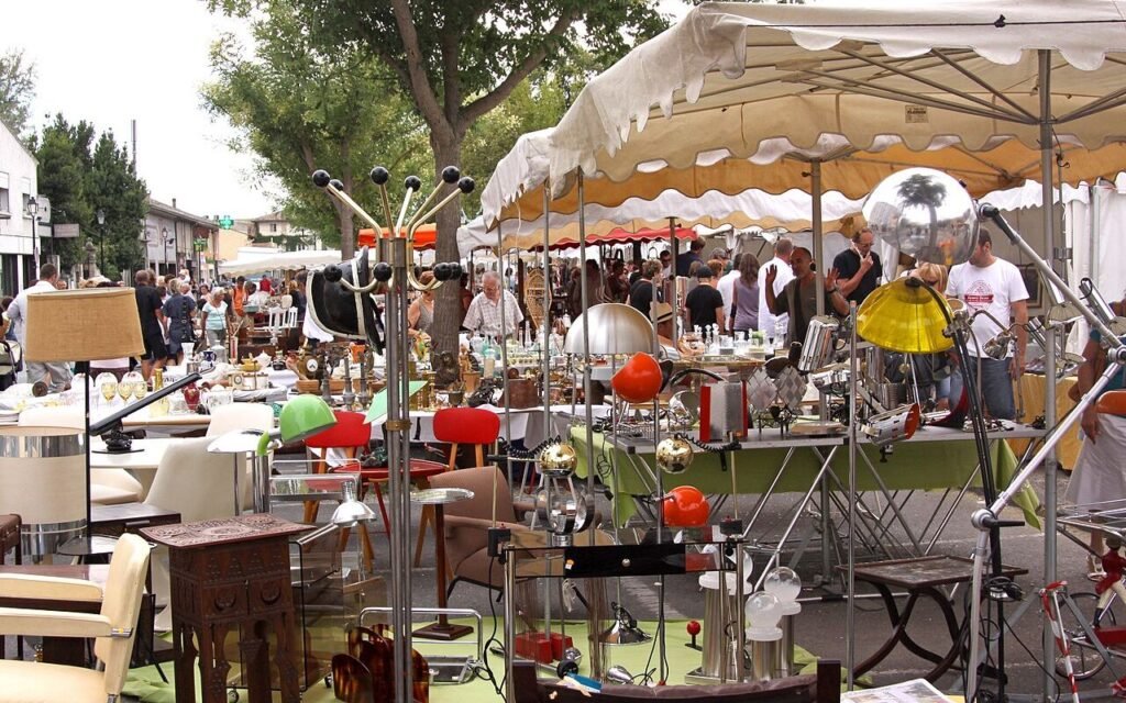 Étals de brocante et d'antiquités sous parasols à L'Isle-sur-la-Sorgue : lampes, luminaires et mobilier ancien