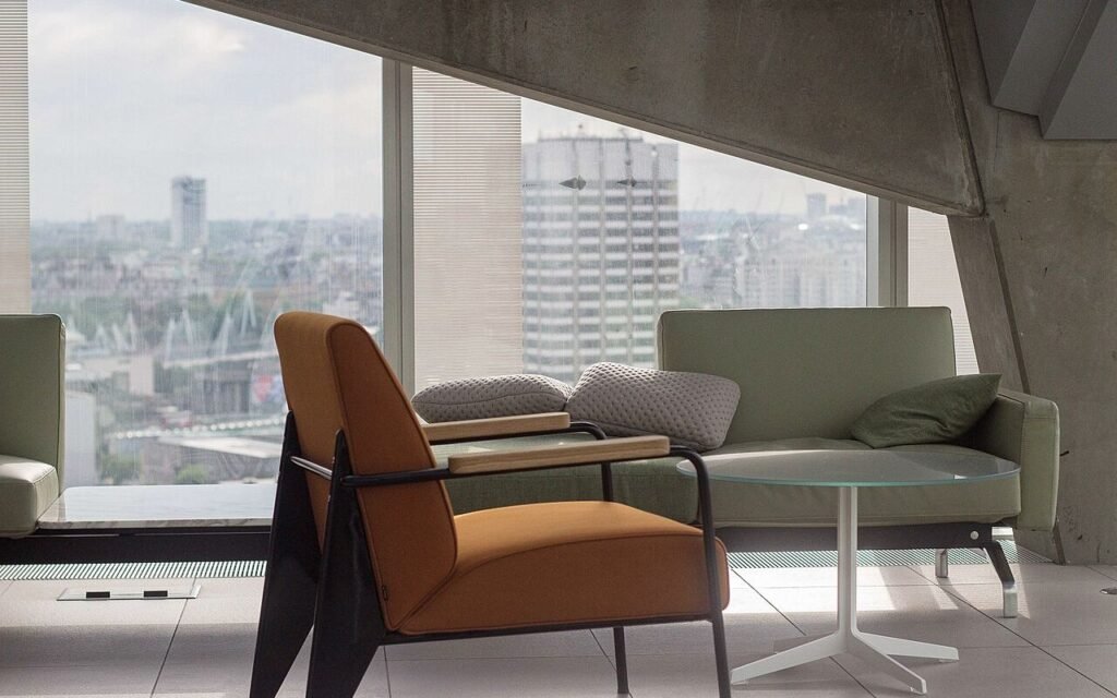 Salon d'appartement meublé avec fauteuil, canapé et grande baie vitrée sur la ville