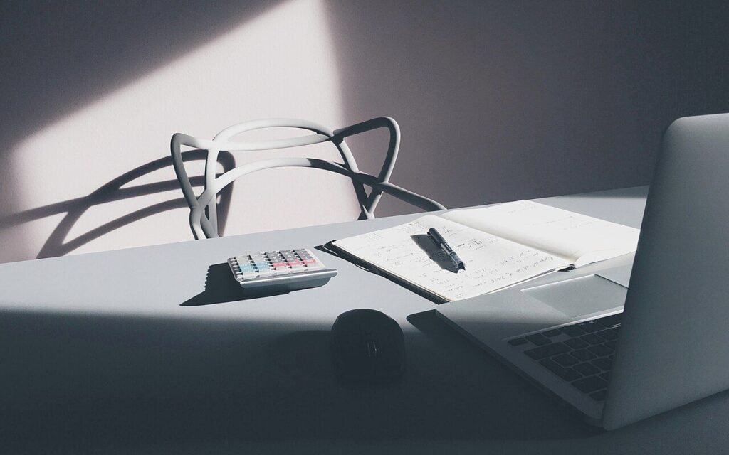 Bureau blanc avec ordinateur portable, calculatrice, carnet ouvert et stylo