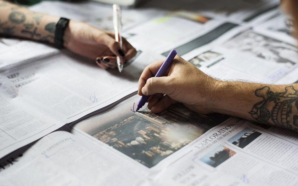 Mains tatouées qui annotent au stylo les pages d'un journal étalé sur une table