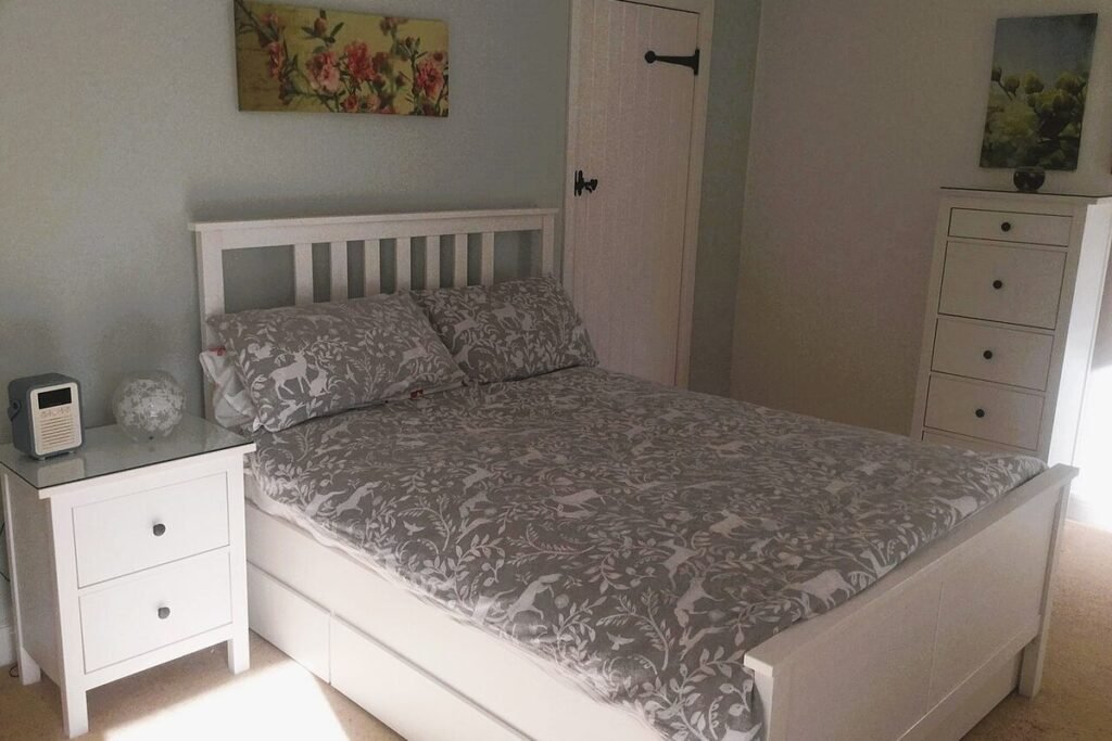 Chambre sobre aux murs gris clair avec lit double, linge gris et tables de chevet blanches