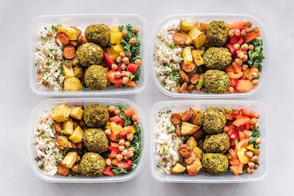 Quatre boîtes repas en verre garnies de boulettes de légumes, de riz et de crudités