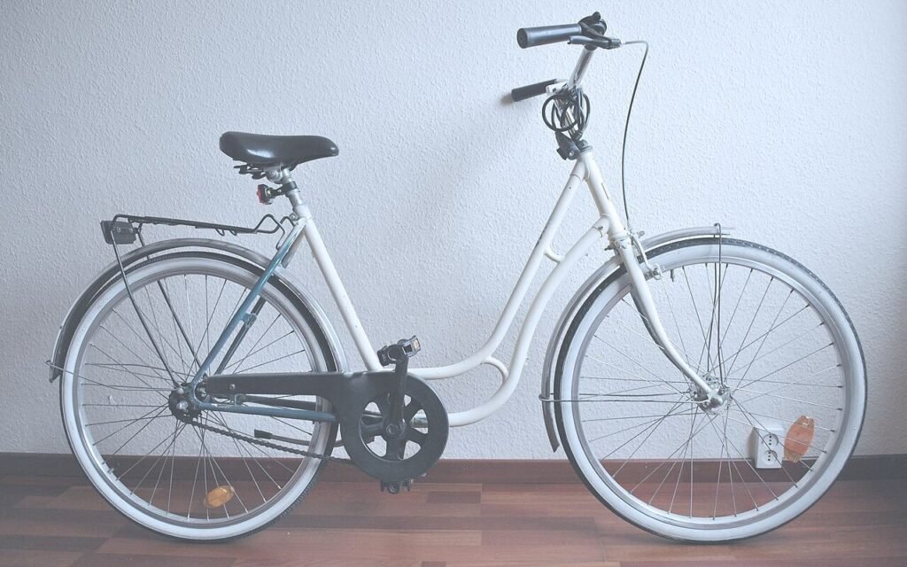 Vélo de ville blanc à cadre bas, avec porte-bagages, posé contre un mur blanc