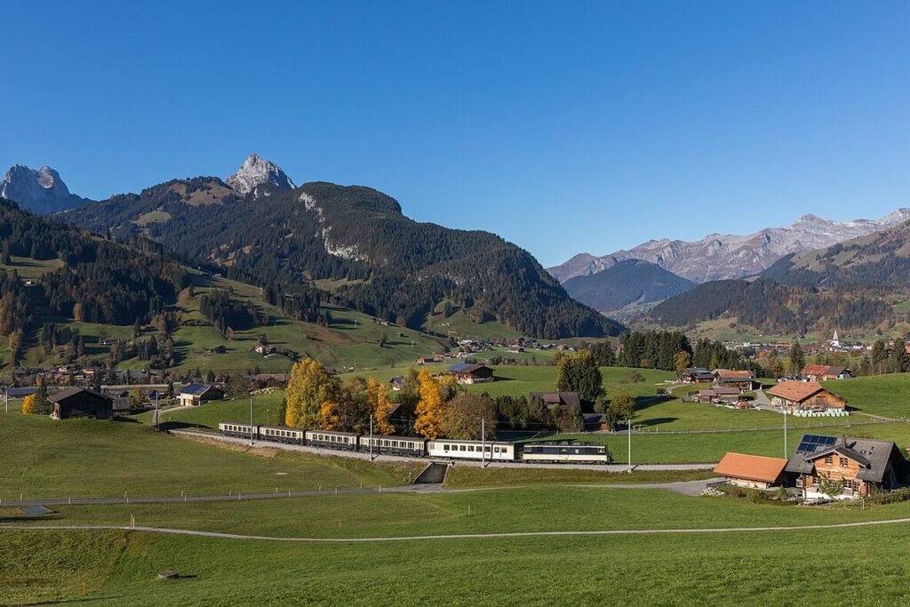 Train panoramique traversant une vallée verte au pied des Préalpes suisses, près de Gstaad